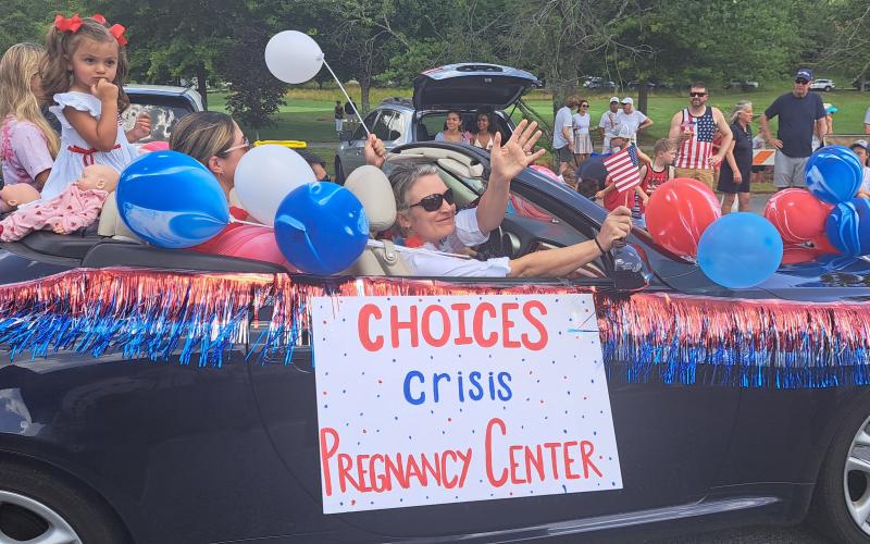 Megan Horn/The Clayton Tribune. Choices Pregnancy Center in the Sky Valley Independence Day Grand Parade. Below: Megan Horn/The Clayton Tribune. Tom DesOrmeaux and Caroline Cobb, 2, don patriotic apparel and wave a flag while awaiting the start of the Sky Valley Independence Day rubber duck race.