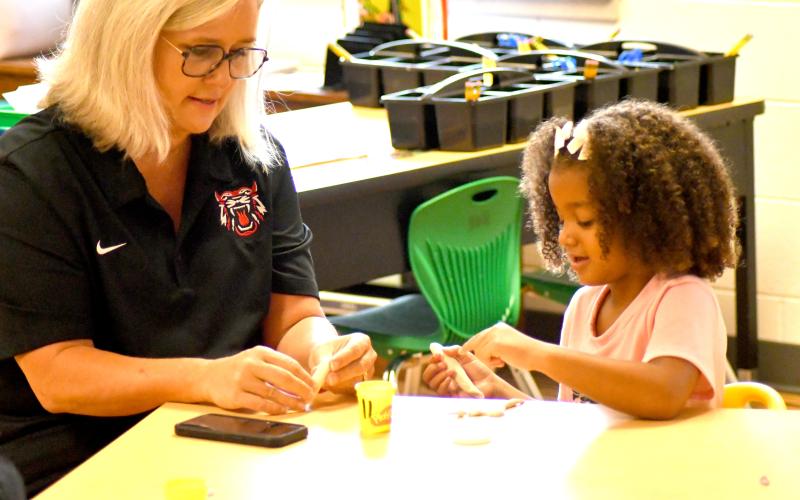 Enoch Autry/The Clayton Tribune. Superintendent Dr. April Childers assists kindergartener Emersyn Fuller with her clay on the first day of school on Tuesday, Aug. 6. Below: School Resource Deputy Sgt. Lindsey Owens directs school traffic on the first day Tuesday, Aug. 6.