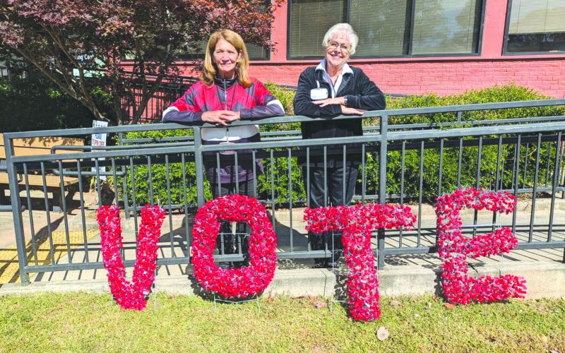 Photo courtesy of Tammy Whitmire. Rabun County Elections Office Poll Workers Kathy Allen, left, and Ann D’Agostino pose in front of this handmade sign encouraging the community to VOTE. D’Agostino made the artwork from the seals taken off of the Ballot Marking Device (BMD) every day.