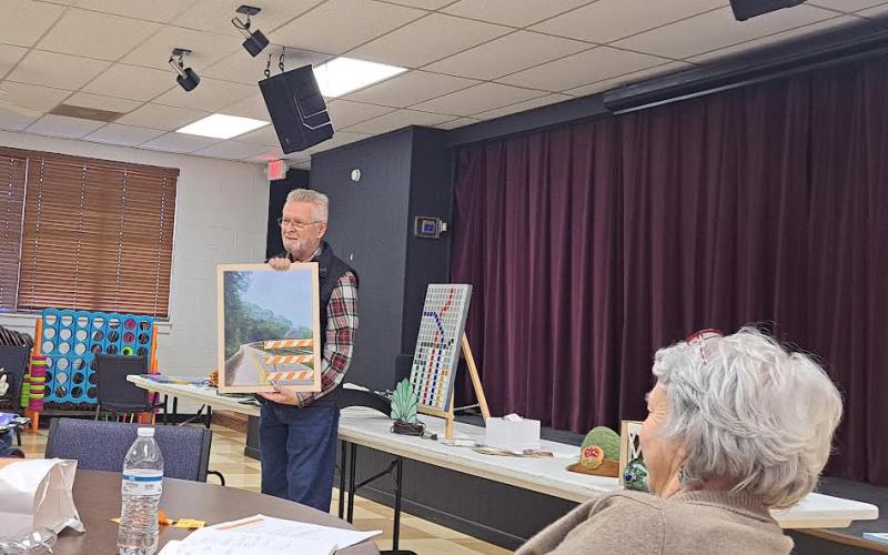 Megan Horn/The Clayton Tribune. Lewis Hinely showcases his artwork at the North Georgia Arts Guild members’ Show and Tell on Oct. 17. Hinely talked about how detours in artwork can be inspired by real life with this painting of a road detour sign. Guild member Kathy Ford is pictured in the forefront. Below:  Joey Aldrich-Burel presents her painting in pastels that was inspired by Vincent Van Gogh.