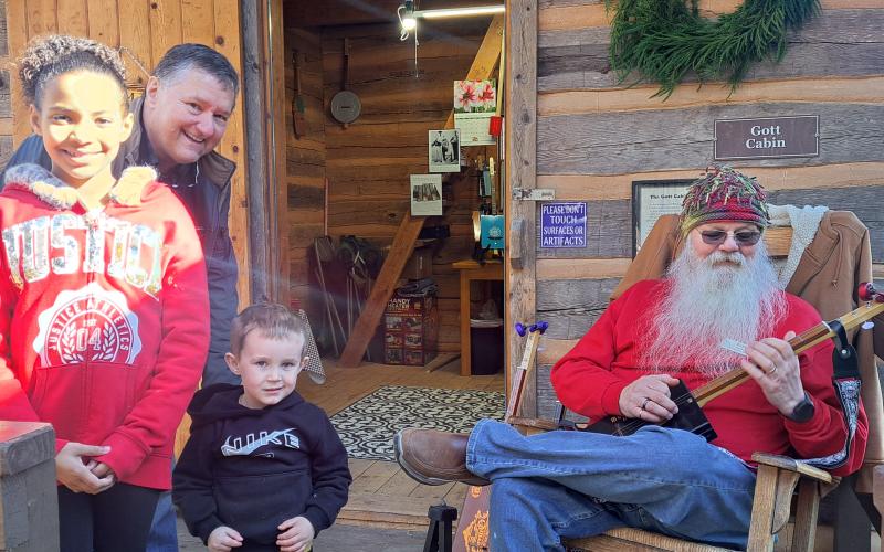Megan Horn/The Clayton Tribune. Les Barnett of Mountain Man Music, right, demonstrates his panjo and canjo creations at Gott Cabin during “A Foxfire Christmas” on Dec. 7. Chris Adams, Kylee Curtis, 9, and Matthew Curtis, 3, learn a lot about instrument making from Barnett.