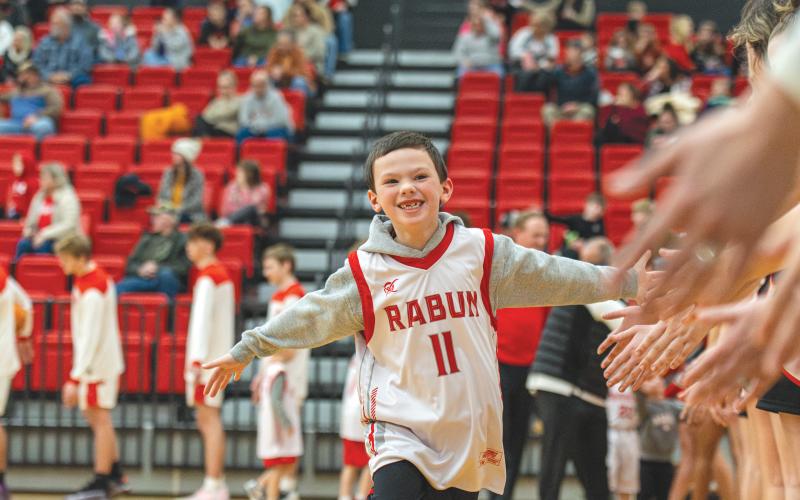 Wade Cheek/The Clayton Tribune. Rave Holcombe, son of RCHS soccer coach Brad Holcombe, runs through the handshake line of varsity basketball players as RCHS honored the community’s rec hoops players on Saturday, Jan. 18.