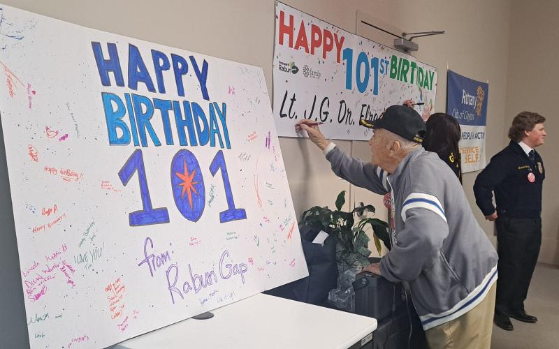 Megan Horn/The Clayton Tribune. Attendees at Tuesday’s Vet-to-Vet Cafe lined up to sign WWII U.S. Navy Veteran Lt. J.G. Dr. Eldred Causey’s “Happy Birthday” banner. Pictured is 100-year-old WWII Army Veteran Andrew “Andy” Negra wishing Causey a Happy Birthday.