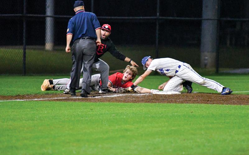 Wade Cheek/The Clayton Tribune. RCHS freshman Chase Alonso hangs onto third base by a thread as he and head coach Wesley Satterfield plead for a safe-call during last Friday’s playoff series against Bremen. Alonso was called safe to confirm a two-run triple.