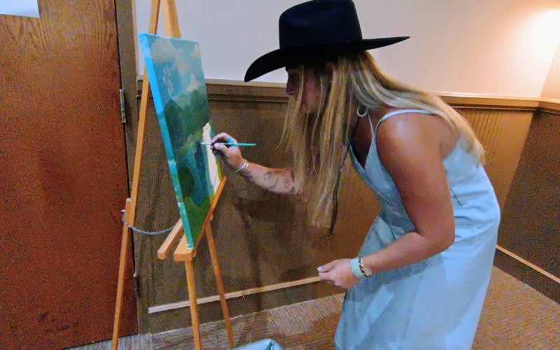 Megan Horn/The Clayton Tribune. Ali Wilkins was seen live painting during the Fur Ball. Her painting of a dog on a lake with a boat in the background sold during the live auction. A painting of a sunny pasture of flowers painted by Tracy McCoy also sold during the live auction. Parker Gonzalez, 19, also painted portraits of attendee’s animals during the Fur Ball to benefit the cause.