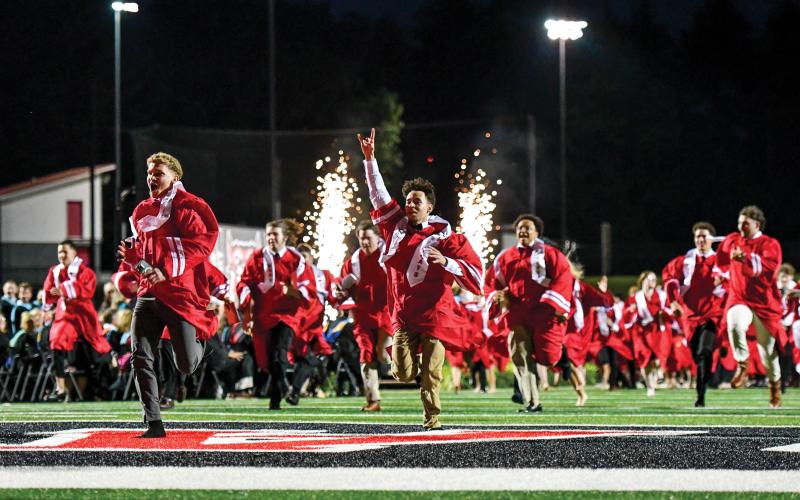 Wade Cheek/The Clayton Tribune. As sparks fly, the Rabun County High School Class of 2025 races to the victory bell at Frank Snyder Memorial Stadium, celebrating their completion of high school.