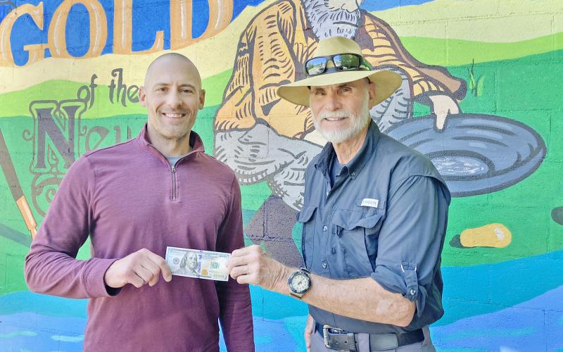 Photo/Keith Murden, CNI News Service. The Dahlonega Nugget Publisher John Bynum (left) presents the $100 prize to Dahlonega resident Bill Perdue for his winning cover photo of a beautiful summer sky above Lake Winfield Scott.