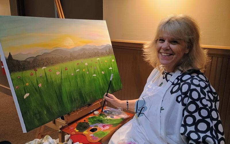 Megan Horn/The Clayton Tribune. Tracy McCoy live paints a sunny pasture of flowers during the Rabun Paws 4 Life event last Saturday. The painting was then sold during the live auction at the end of the night. Local artist Ali Wilkins was also seen live painting during the Fur Ball. Her painting of a dog on a lake with a boat in the background sold during the live auction. Parker Gonzalez, 19, also painted portraits of attendee’s animals during the Fur Ball to benefit the cause.