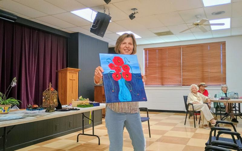 Megan Horn/The Clayton Tribune. Allyson Aldrich showcases her colorful painting featuring “Abstract Poppys” during the North Georgia Arts Guild “Members’ Show and Tell” program July 17. The painting is primarily acrylic and is finalized using spoons. She calls these creations “spoon art.