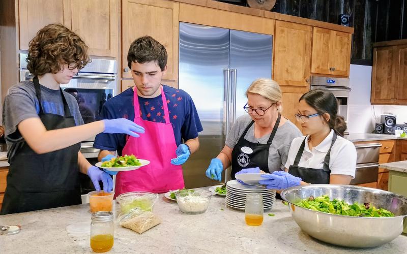 Megan Horn/The Clayton Tribune. Local students recently got the opportunity to participate in an Advanced Cooking Class as part of the Food Bank of Northeast Georgia Teaching Kitchen Program. Pictured are Tessa Stuckey; Hank Stuckey; Kitchenette Volunteer Annette Branan; and Tara Shryock plating an Irish flag salad with homemade dressing for the July 25 four-course meal prepared for their favorite adults at the Teaching Kitchen.