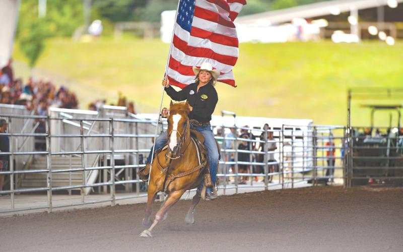 Wade Cheek/The Clayton Tribune. Jamie Ellsworth rides through Rabun Arena with the Stars and Stripes during the opening ceremonies of the Rabun Arena Rodeo 2024 Fourth of July weekend.