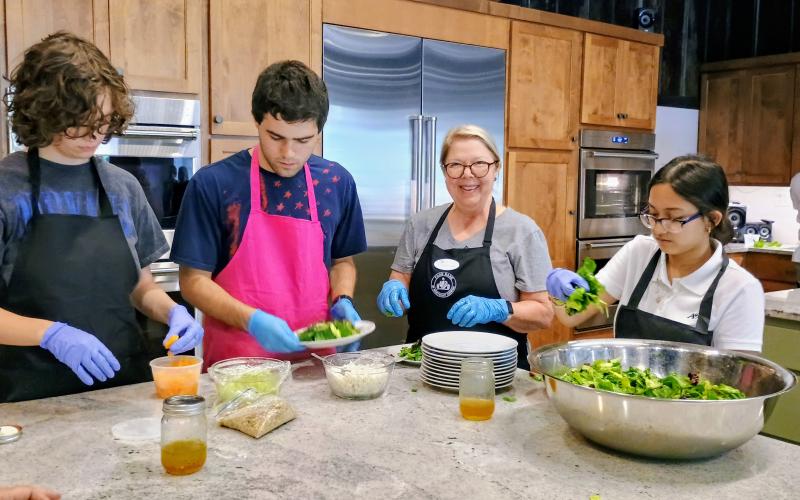 Megan Horn/The Clayton Tribune. Tessa Stuckey; Hank Stuckey; Kitchenettes Volunteer Annette Branan; and Tara Shryock work to prepare an Irish flag salad with homemade dressing during the July 25 dinner at the Teaching Kitchen. A four-course meal prepared by students culminated three days of an Advance Cooking Class as part of the Teaching Kitchen program.