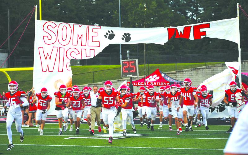 Enoch Autry/The Clayton Tribune. The Rabun County cheerleaders continued their tradition of creating special banners for each Wildcat football game so the team can run through them onto the football field. Here the players and first-year head coach Rance Gillespie (left center) make their way toward the home sideline during pregame of the Aug. 8 scrimmage against visiting Franklin, N.C.