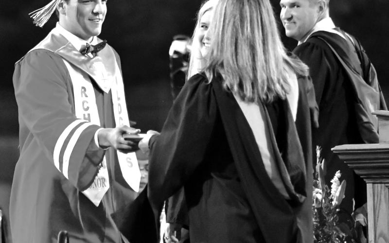 Enoch Autry/The Clayton Tribune. Rabun County High School Principal Justin Spillers (far right) and then Superintendent Dr. April Childers smile as Class of 2022 honor graduate and record-setting Wildcat quarterback Gunner Stockton receives his diploma in May 2022 from his mother Sherrie Stockton, then a RCHS counselor.