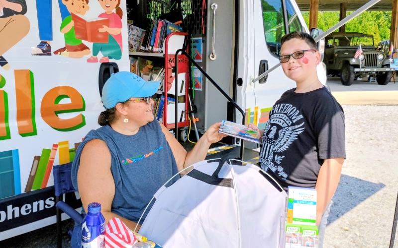 Megan Horn/The Clayton Tribune. The Northeast Georgia Regional Library System Bookmobile was on site at the Rabun County Fuller Center for Housing “Touch-A-Truck” event last weekend. Jenny Brooks, outreach and Bookmobile manager, helps Matthew Ramey, 10, check out a book from the Bookmobile.