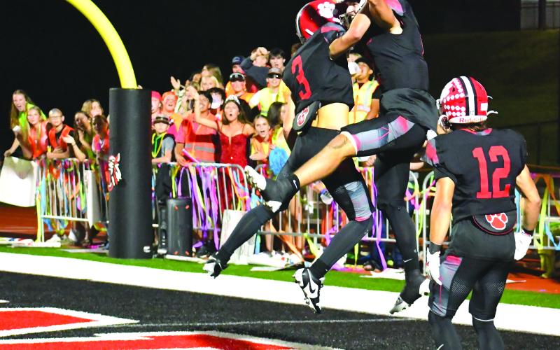 Enoch Autry/The Clayton Tribune. Rabun County senior quarterback Ty Truelove celebrates with freshman Cooper Kowalsky (3) after the signal caller runs 69 yards for a touchdown. The score by Truelove was his fifth TD of the night against Banks County in the Homecoming win. In the background, the RCHS student section cheers on their Wildcats. In the front is Hayden Bass, who was crowned as the 2025 Homecoming Queen at halftime.