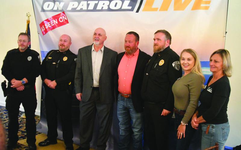 Enoch Autry/The Clayton Tribune. Clayton police officers and Clayton council members and staff pose for a photograph with Hazen (Ark.) Police Chief Bradley Taylor (center) during his Oct. 17 visit to Rabun County as part of the Rabun County Chamber of Commerce Business Breakfast. Taylor is a regular on the television show “On Patrol: Live.”