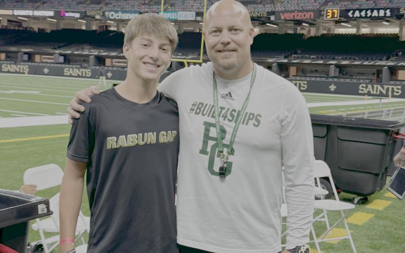 Submitted Photo. Rabun Gap head football coach Derek White poses with his son Asa before a game versus John Curtis Christian in New Orleans in September 2024. Asa, now a freshman at Rabun Gap, plays defensive back for the Eagles.