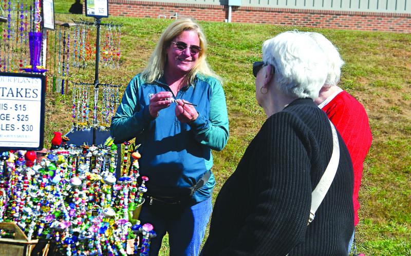 Enoch Autry/The Clayton Tribune. Danette Peters (center) of Why Knot Designs of Blairsville, Ga., talks with customers at the Nov. 1 Of These Mountains Fall MarketPlace on the Rabun County Civic Center Pavilions property. Why Knot Designs was one of the 120 booths that set a record for vendors at the event at the height of “Leaf Season.”