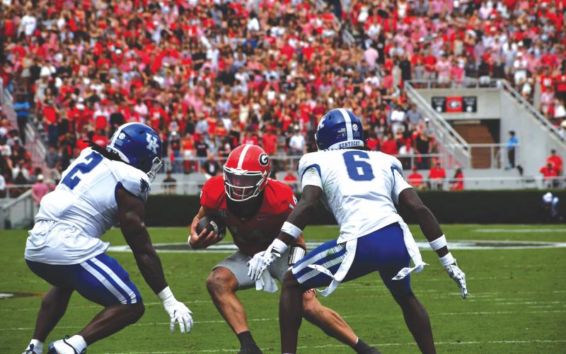 Wesley Branch/The Clayton Tribune. Former Rabun County and current UGA quarterback Gunner Stockton evades two defenders in Georgia’s 35-14 win over Kentucky on Oct. 4. Stockton helped lead Georgia to a second consecutive SEC title in his first full season as the starting QB.