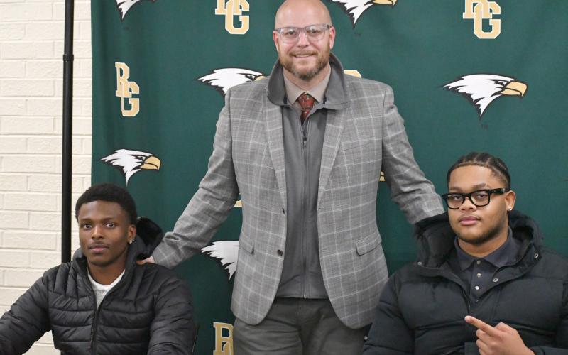 Wesley Branch/The Clayton Tribune. Rabun Gap head football coach Derek White (center) poses with Rabun Gap seniors CJ Willingham (left) and Devon Holly (right) on Feb. 5 at Rabun Gap’s signing day recognition for Willingham and Holly. Willingham will continue his football and academic careers at Columbia University, while Holly signed to North Carolina A&amp;T.