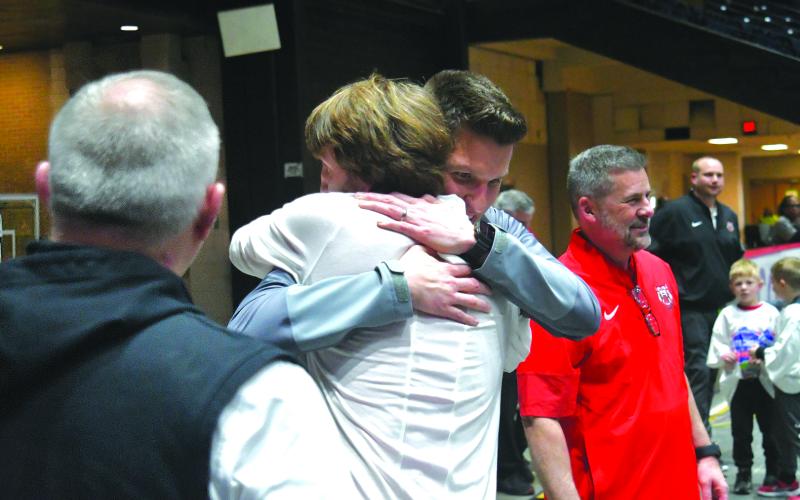 Enoch Autry/The Clayton Tribune. Rabun County head coach David Adcock receives a hug from RCHS Principal Justin Spillers after the Wildcats win the state title on March 13. In the foreground is Athletic Director Jonathan Welch. To the right are Superintendent Steven Cole and assistant boys basketball coach Corey Page.