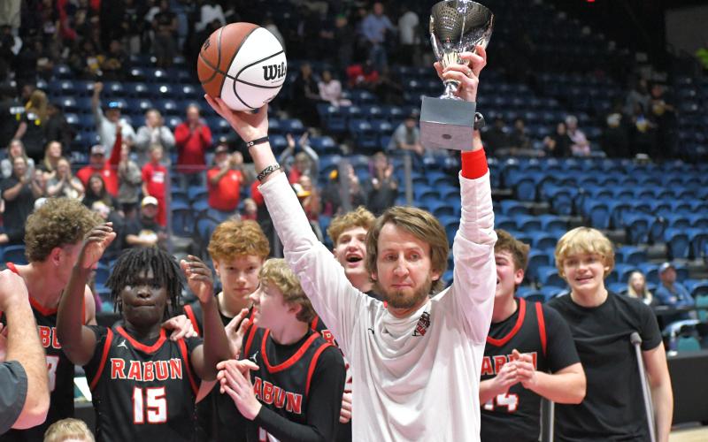 Wesley Branch/The Clayton Tribune. RCHS head coach David Adcock holds up the trophy and game ball as the Class A Division I state champions while his team celebrates the achievement.