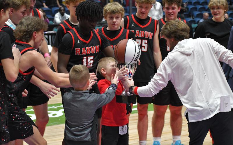 Wesley Branch/The Clayton Tribune. RCHS head coach David Adcock hands the state championship trophy and basketball to Cal Burrell and Reeves Page as senior Colton Crane (left) moves in to help the “goons” lift the two important pieces of hardware.