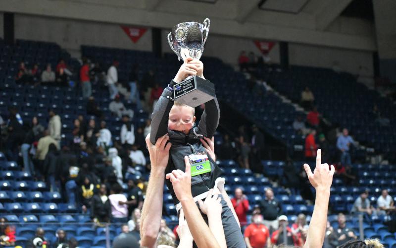 Wesley Branch/The Clayton Tribune. The Rabun County boys basketball team lifts Reeves Page, the son of assistant coach Corey Page, in celebration with the championship trophy after the team’s 52-43 state title victory over Southwest on March 13 at the Macon Coliseum. The championship is the first in the history of the boys basketball program.