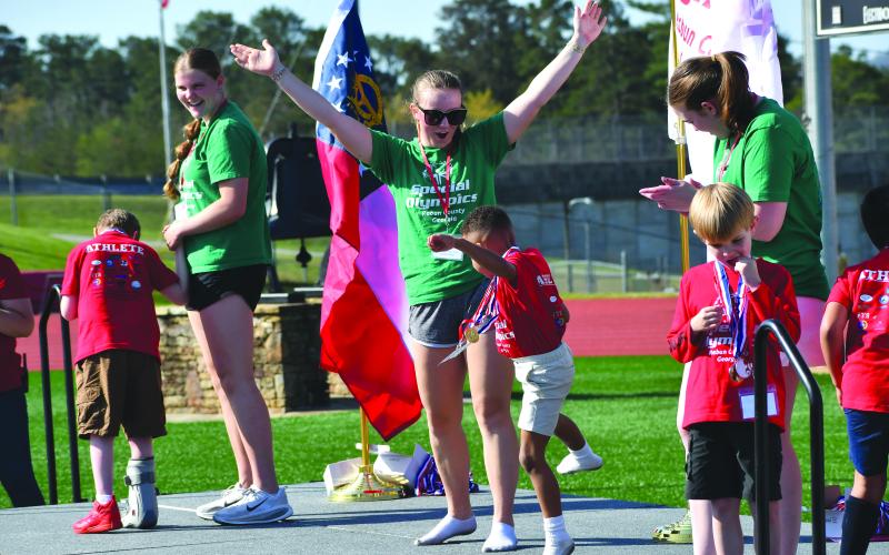 Wesley Branch/The Clayton Tribune. Adrian Appleby (center) dances on the stage with buddy and Rabun County High School student Bella Hulsey after receiving a medal at the Rabun County Special Olympics on April 2 at Frank Snyder Memorial Stadium. Also on the stage receiving medals as photographed above are athletes Truett Beck (right) and Jonathan Chapman (left) with buddies Katelynn Duncan and Chloe Shirley.