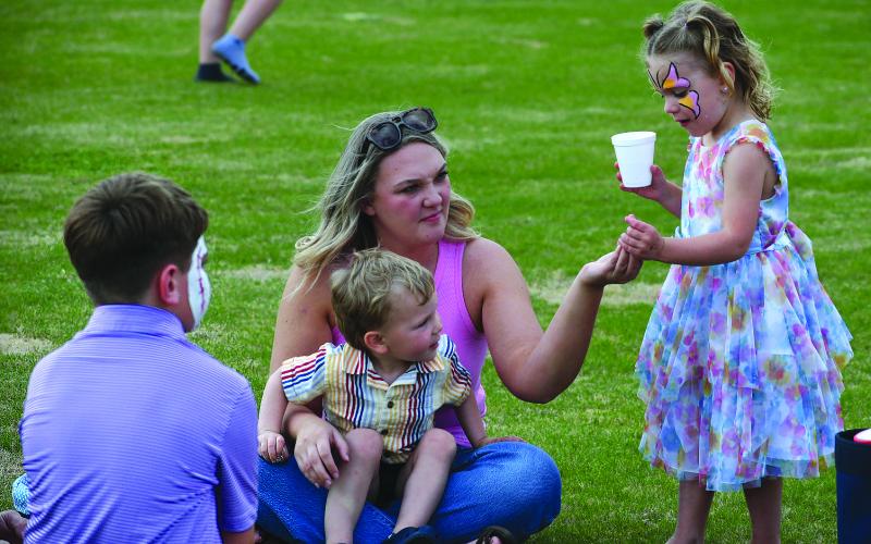 Enoch Autry/The Clayton Tribune. While sitting with her 2-year-old son Henry Gibson, Kelli Barnes hands a small yellow ball to 4-year-old Piper Gragg as 9-year-old Walker Gragg (foreground) watches as the games are being run prior to the start of the April 2 Egg Hunt at the Rabun County Recreation Department. Barnes is a family friend of the Graggs.