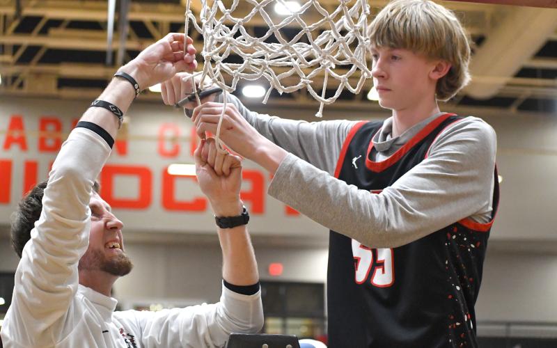 Wesley Branch/The Clayton Tribune. Rabun County head boys basketball coach David Adcock cuts down the net with his son RCHS freshman Trace Adcock at the Rabun County High School boys basketball state championship celebration on March 26 on the school’s campus. Coach Adcock played at RCHS for his father, Mike, and is now coaching a third generation of Adcocks to play at Rabun County.