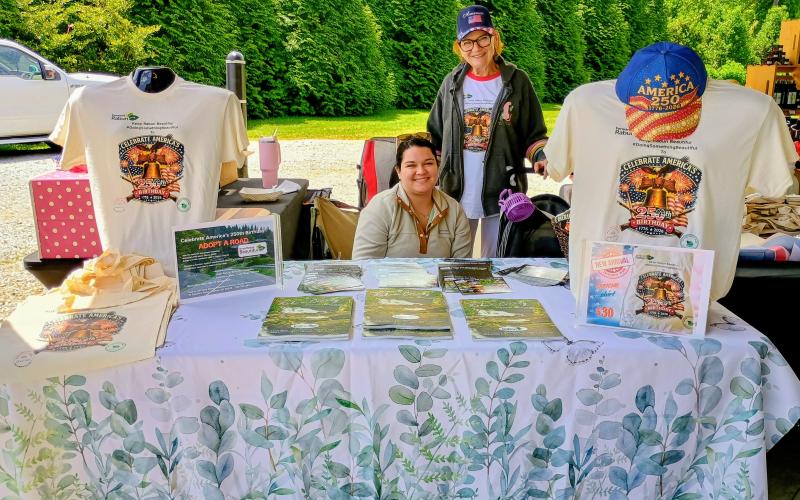 Megan Horn/The Clayton Tribune. Madison Marcus and Linda Scofield, Rabun County Welcome Center manager, greet visitors to the Of These Mountains Spring MarketPlace May 9 and encourage them to celebrate America’s 250th birthday and Adopt a Highway.