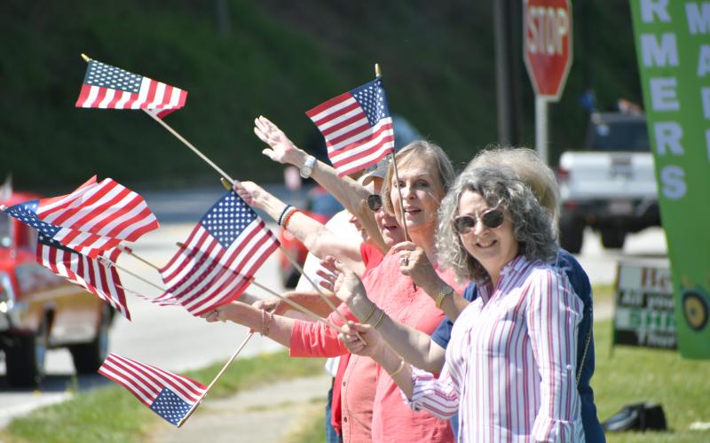 Enoch Autry/The Clayton Tribune. A group of patriotic residents wave American flags at the passing convoy on the Highway 441 sidewalk near the Food Bank of Northeast Georgia.