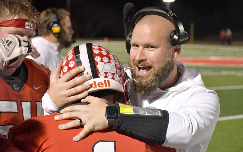 Wesley Branch/The Clayton Tribune. Rabun County running backs coach Clay Worley hugs Rabun County running back Lake Evans after a touchdown run in RCHS’ 35-0 playoff win over Berrien on Nov. 21, 2025.