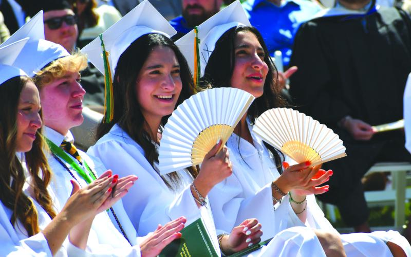 Enoch Autry/The Clayton Tribune.  Twins Irmak Bilici and Pinar Bilici smile and use hand fans on a warm morning on the Rabun Gap campus for the commencement.