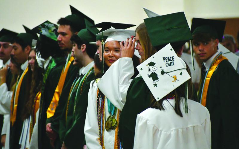 Enoch Autry/The Clayton Tribune.  Jessica Cook’s mortar board on her graduation cap is decorated with “Peace Out!” with the likeness of Snoopy and Woodstock as she and her fellow seniors stand in the front row of the group of the Class of 2026.