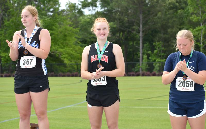 Wesley Branch/The Clayton Tribune. Rabun County freshman Irie McElroy (center) smiles after receiving her medal for earning fourth place in the girls discus at the GHSA state championship meet on May 12 in Athens. McElroy set a RCHS school record in the event earlier in the season.