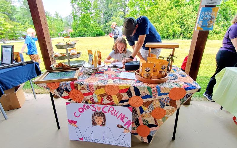 Megan Horn/The Clayton Tribune. Cora Rose and Ben Rose sell products from the business “Cora’s Crunch.” The idea for the convenient snack, which comes in flavors Campfire crunch and Classic crunch, was inspired by hikers in Rabun County because it’s a simple snack hikers can carry with them.