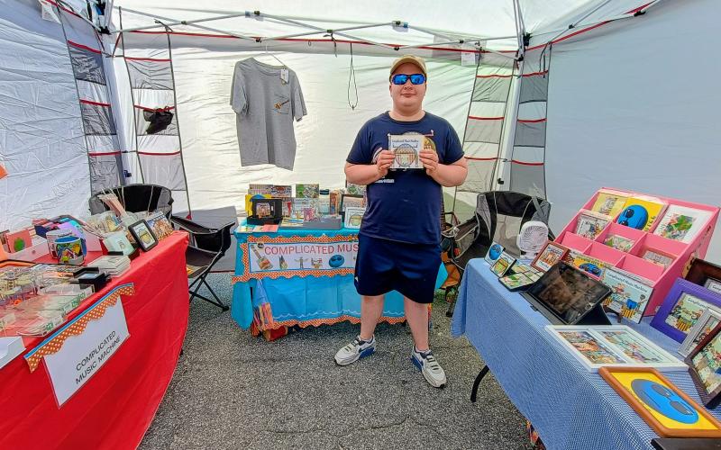 Megan Horn/The Clayton Tribune. Jacob Ray is the creater/bandleader for Complicated Music Machine. He showcases his merchandise to visitors at Ramshackle. Complicated Music Machine is America’s next famous virtual band.