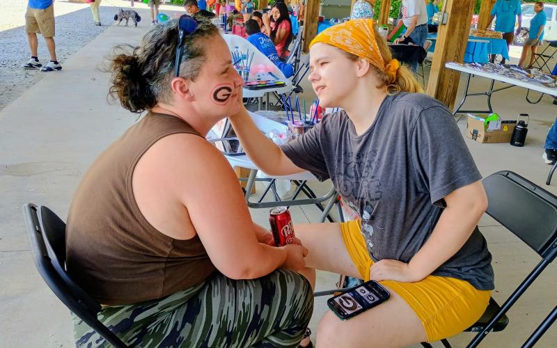 Megan Horn/The Clayton Tribune. Laura Ivey paints the face of Kayla Hughes during a Community Celebration held at the pavilions behind the Rabun County Civic Center last weekend. The free event was sponsored by the Rabun County Association of Southern Baptist Churches.  It featured bouncy games, balloon animals, car show and ice cream.