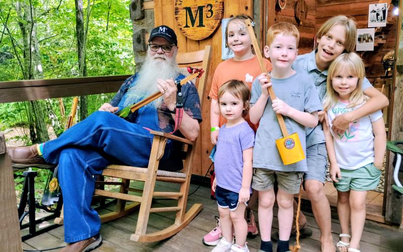 Megan Horn/The Clayton Tribune. Les Barnett with Mountain Man Music Custom Guitars showcases his unique panjos and canjos to kids at Foxfire Heritage Days. Barnett demonstrates his musical instruments to Chesney Godwin, 8; Tio O’Connell, 10; Astra O’Connell, 4; Emmy Kate, 2; and Henry Godwin, 5.
