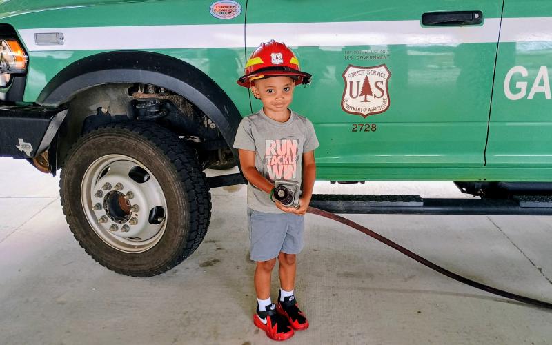 Megan Horn/The Clayton Tribune. AJ Appleby, 5, wears a firefighter helmet and holds a fire hose during a Tuesday, June 9 Rabun County Public Library summer program with the U.S. Forest Service and Smokey Bear.