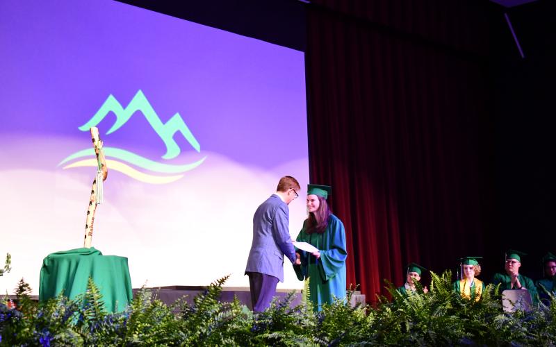 Megan Horn/The Clayton Tribune. Ora Bella Davis, Rabun Mountain Education Class of 2026 graduate, shakes hands with Rabun Mountain Education Campus Principal Allen Blair and accepts her diploma as she walks across the stage on May 23.