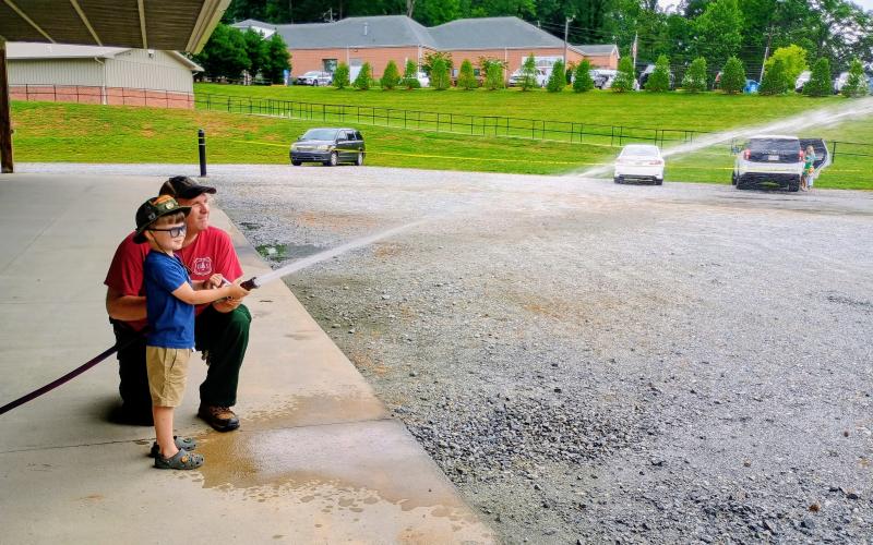 Megan Horn/The Clayton Tribune. Olin Houser, 4, sprays the hose with Wildland Firefighter Thomas assisting, during the Smokey Bear event at the pavilions in Clayton.