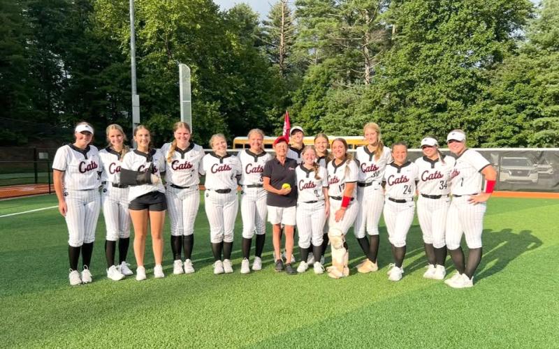 Submitted Photo. Former Rabun County High School teacher and coach Janice Wayne (center) poses with the Rabun County softball team after throwing the first pitch at a game during the 2025 season. Wayne, the first-ever softball coach at RCHS who also assisted athletics in a plethora of ways, passed away on June 24 at the age of 72.