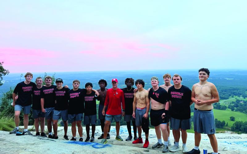 Wesley Branch/The Clayton Tribune. The Rabun County Class of 2027 football seniors stand with head coach Rance Gillespie (center) for a photo as the sun rises on Currahee Mountain. The Wildcats hiked three miles up the mountain in the early morning hours, following their midnight practice.