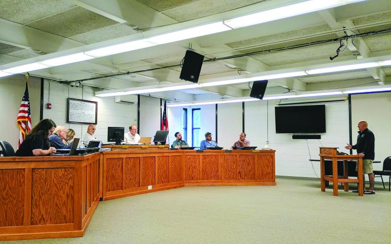Megan Horn/The Clayton Tribune. Moonrise Distillery owner Doug Nassaur, far right, talks to Clayton City Council members on July 14 about delinquent taxes reported by the city. Nassaur addresses (from left) City Manager Kessiah Gipson, Council Member Tony Allen, City Manager Trudy Crunkleton, Mayor Roy Quilliams, City Attorney Mitch Baker, and council members Colt Woodall, Channing Watts and Stacy Fountain.