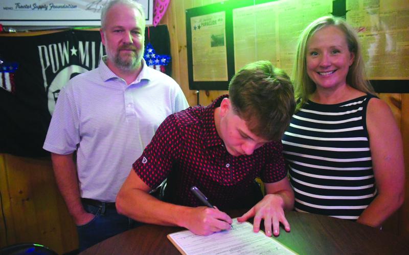 Wesley Branch/The Clayton Tribune. Huey Blalock (center) signs documents for his enrollment into the Naval Academy alongside his parents Woody Blalock (left) and Katrina Blalock (right) at VFW Post 4570 in Clayton on June 24. Blalock signed his letter of intent to play basketball at Navy in late April and recently graduated from Rabun County High School.