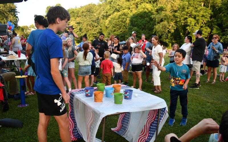 Megan Horn/The Clayton Tribune. Moises Lopez, 7, throws a ball into a cup at one of the many kids’ activities at the July 1 Stars Over Clayton inaugural event. Pictured left is volunteer Levi Stockton, 16.
